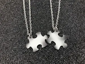 Polished stainless steel interlocking puzzle piece necklaces on glitter background