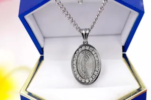 Close-up of oval Virgin Mary pendant necklace with rhinestone border in a blue gift box