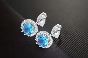 Close-up of silver stud earrings with blue zircon center and halo of white stones.