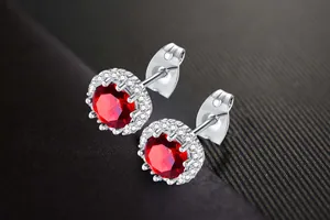 Detail of round red birthstone stud earrings with white halo stones in silver