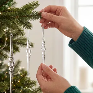 Nahaufnahme von Händen, die klare Acryl-Eiszapfen an den Weihnachtsbaum hängen