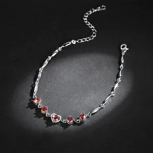 Macro detail showing heart-shaped red zircon stones on a silver-toned delicate bracelet