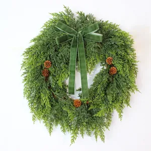 Detailed view of lush green artificial cedar wreath with velvet bow and rustic pine cones.