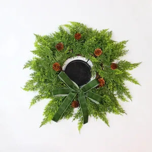 Artificial Christmas cedar pine wreath decorated with cones and a green velvet bow