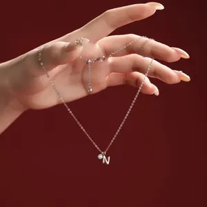 Detailed close-up of a silver necklace with N letter pendant and small sparkling stone.