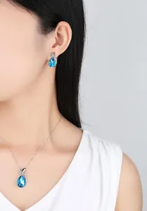 Close-up detail of an elegant blue teardrop crystal necklace and earring jewelry set on a model