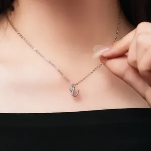 Detail view of dainty silver letter U pendant necklace with sparkling stone worn by a model