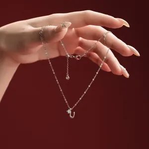 Close-up of a hand holding a silver letter U pendant necklace on a red background