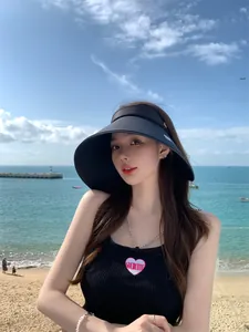 Vrouw met zwarte zonneklep met brede rand op een zonnig strand, ideaal voor de zomer