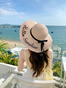 Γυναίκα με κομψό ψάθινο καπέλο με κέντημα Hello Sunshine σε ένα ηλιόλουστο παραθαλάσσιο