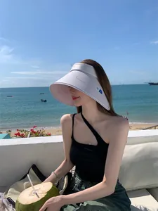 Model met een witte UPF 50+ zonneklep met brede rand voor een zonnige strandachtergrond