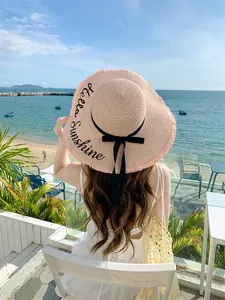Πίσω όψη γυναίκας με ροζ ψάθινο καπέλο Hello Sunshine κεντημένο σε παραθαλάσσια βεράντα