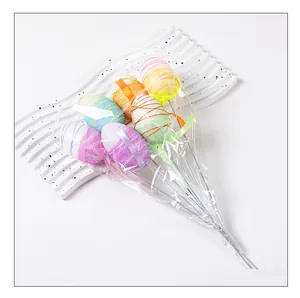 Bastoncini colorati per uova di Pasqua avvolti in plastica su vassoio bianco.