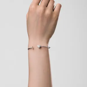 Nahaufnahme eines silbernen Herz-Armreifs am Handgelenk mit minimalistischem Design