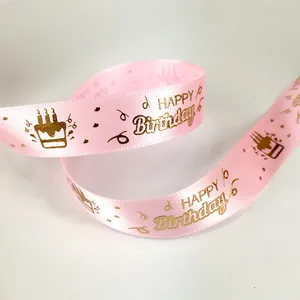 Close-up of pink satin ribbon with gold foil Happy Birthday text and cake icons.