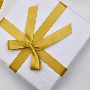 Elegant 1.5cm golden yellow polyester ribbon tied in a bow on a white textured gift box