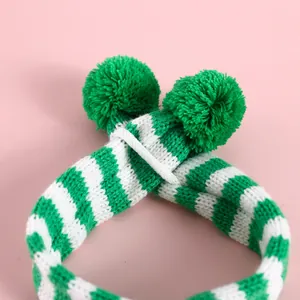Détail macro d'une écharpe tricotée rayée vert et blanc pour animaux avec pompons.