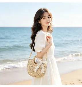 Close-up of semi-circular woven straw bag with white lace bow on sunny beach