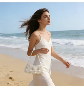Model trägt eine elegante weiße Perlen-Umhängetasche an einem sonnigen Sandstrand