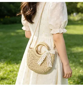 Woven semi-circular straw bag with decorative lace bow shown on a model in a garden setting
