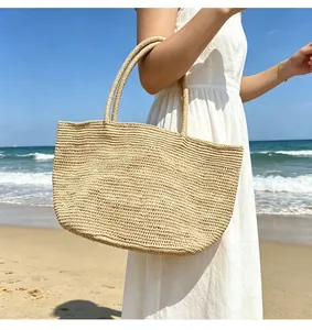 Große gewebte Bast-Tote-Bag am sonnigen Sommerstrand am Meer in der Hand gehalten