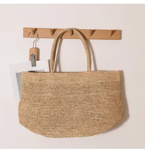 Detail einer handgewebten Bast-Tragetasche, die an einem Holzhaken für den Strandurlaub hängt