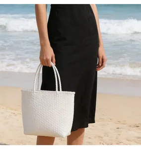 Detailed view of a white woven plastic tote bag held by a model on a sunny beach