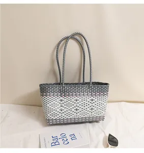 Dettaglio di una borsa da spiaggia in plastica intrecciata grigia e bianca con manici.