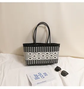 Vista dettagliata di una borsa tote intrecciata bianca e nera con occhiali da sole e libro.