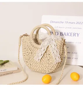 Detail view of a woven straw crossbody bag featuring a white lace bow and top handles