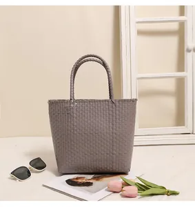 Close-up of a grey woven plastic tote bag with sunglasses and flowers on a white surface