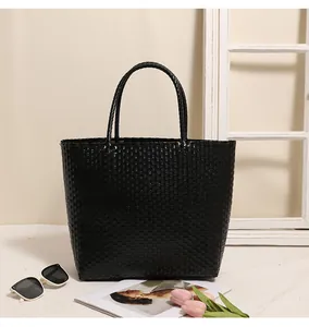 Black woven plastic tote bag styled with sunglasses and tulips on a beige surface