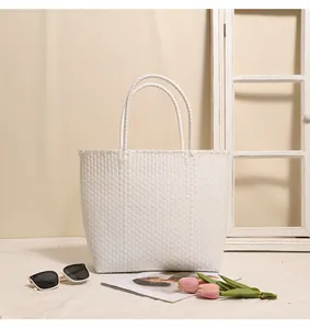 White woven plastic tote bag styled with sunglasses and tulips on a table