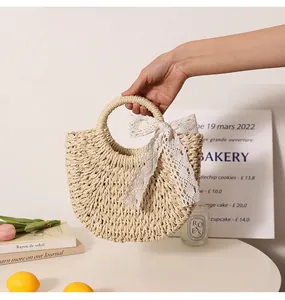 Hand-held view of the half-moon straw bag with elegant white lace bow detail.