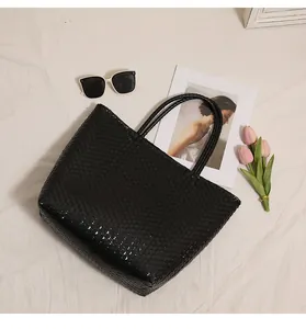 Close-up detail of the hand-woven plastic texture on this stylish black beach tote bag.