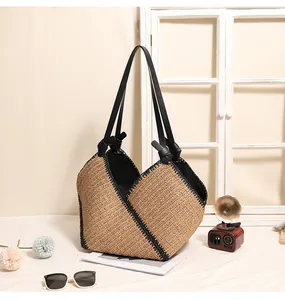 Lifestyle view of a large woven straw tote bag with black trim and knotted straps.