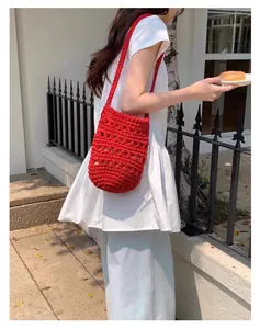 Modelo con un bolso tipo cubo de algodón de ganchillo rojo en ambiente exterior