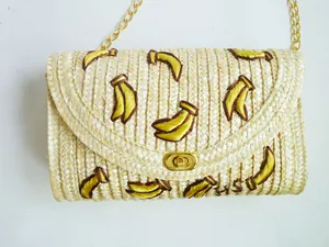 Detail van handgeborduurd bananenpatroon op een strooien schoudertas met gouden ketting