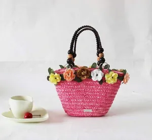 Detailweergave van een roze strooien strandtas met bloemendecor en houten kralen