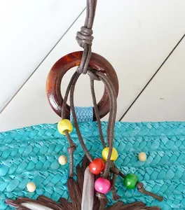 Close-up detail of a blue woven straw beach bag with colorful beads and wooden ring.