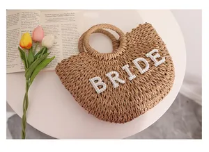 Detalle de bolso de playa de paja trenzada con letras 'BRIDE' decoradas con perlas