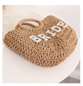 Detalle de un bolso de paja trenzada con las letras BRIDE decoradas con perlas finas.