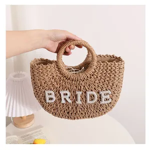 Vista detallada del bolso de paja semicircular con letras BRIDE de perlas para bodas.