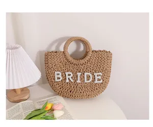 Detalle de un bolso de paja tejido semicircular con elegantes letras BRIDE de perlas.