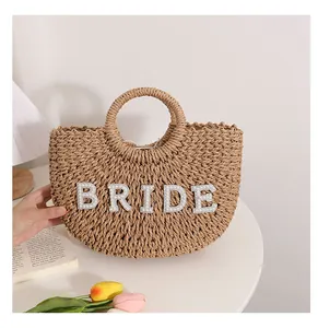 Detalle de bolso de paja trenzada con letras BRIDE de perlas para bodas en la playa