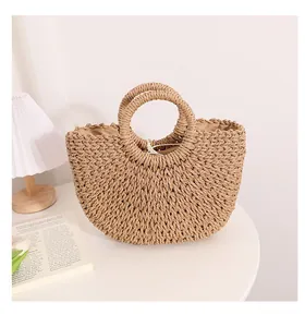Bolso de paja tejida en forma semicircular sobre mesa blanca para playa o vacaciones