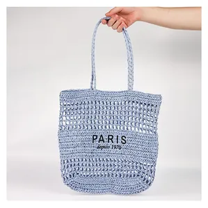 Vue rapprochée d'une main tenant un sac cabas en paille évidée avec broderie Paris
