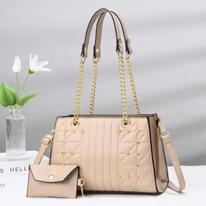 Beigefarbene Stepphandtasche mit Goldketten und Perlenverzierung im Studio-Ambiente