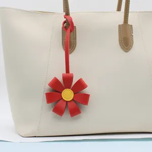Close-up detail of a vibrant red 3D PU leather flower charm hanging on a white tote bag.