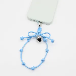 Detail view of a blue braided phone wrist strap featuring a bow and heart pendant charm.